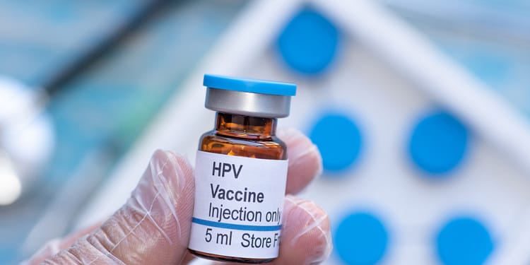 HPV vaccine vial in a gloved hand, labeled "Injection Only" and with a volume of 5 mL.
