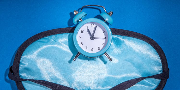 Blue alarm clock on a light blue sleeping mask, on a blue background.