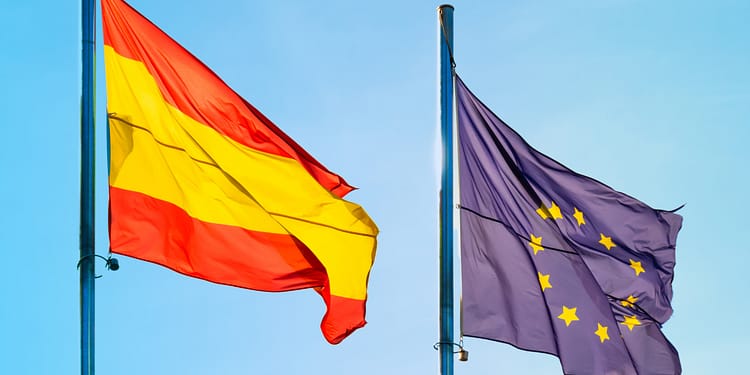Flags of Spain and the European Union waving in a blue sky.