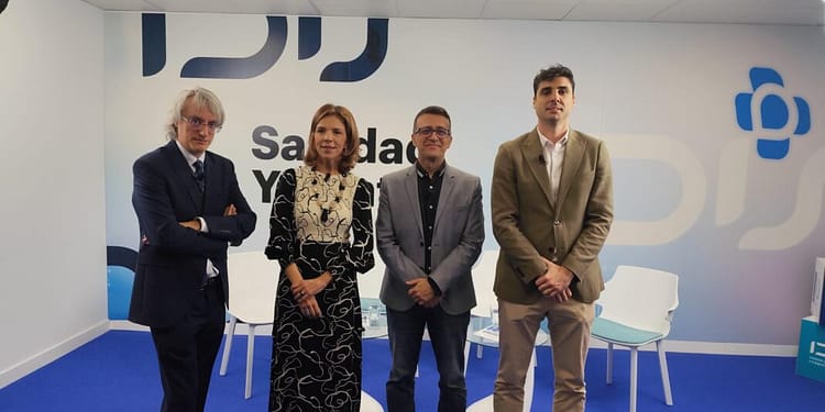 Cuatro personas de pie en un fondo con el texto "Salud y bienestar". Dos hombres con trajes y dos mujeres, una con un vestido largo negro y blanco, y la otra con blusa y pantalones. El ambiente es moderno y acogedor.