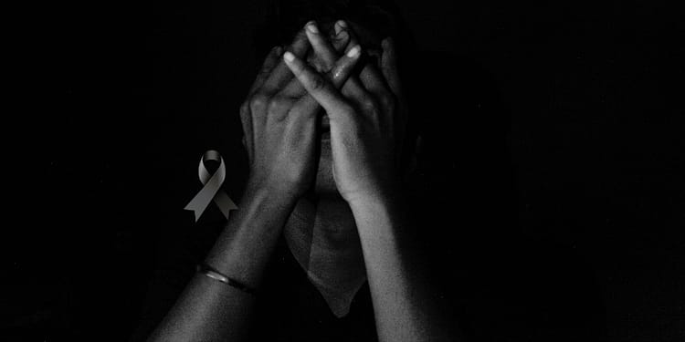 A person with their hands on their face, in a dark environment, with a black bow superimposed on the image.