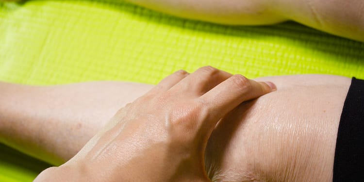 A hand gently presses a person's knee against a bright green surface.