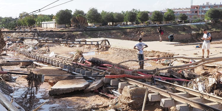 Disaster zone with debris and fallen cables, people inspect the area affected by floods.