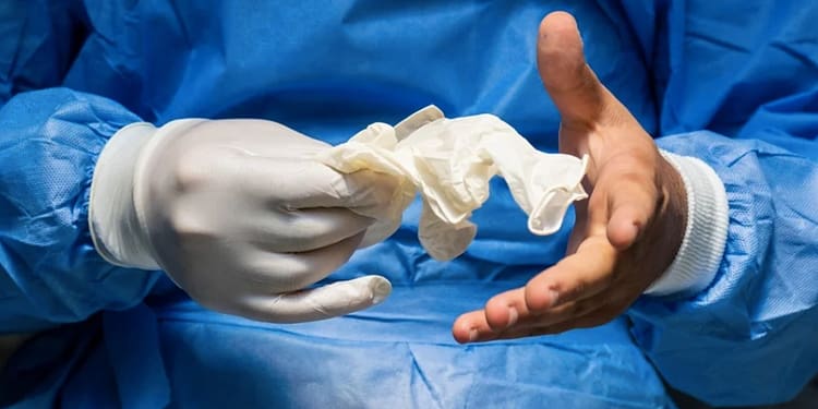 Mano con guante de látex sosteniendo un guante desechado, en un entorno sanitario.