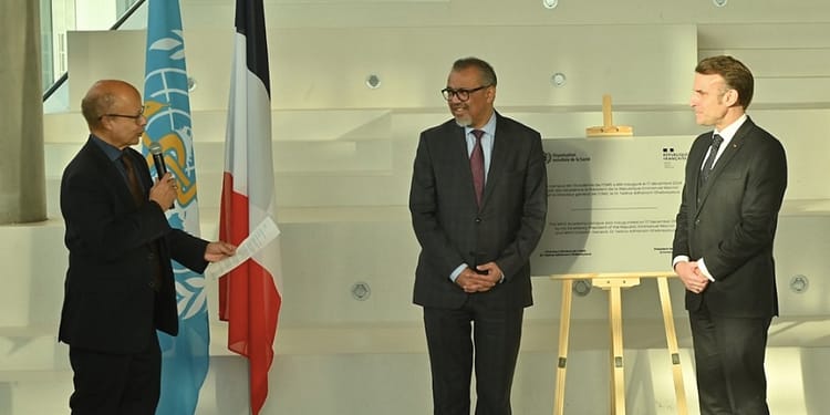 Ceremony with three men at an official event, with UN and French flags in the background, and an information panel about a project.