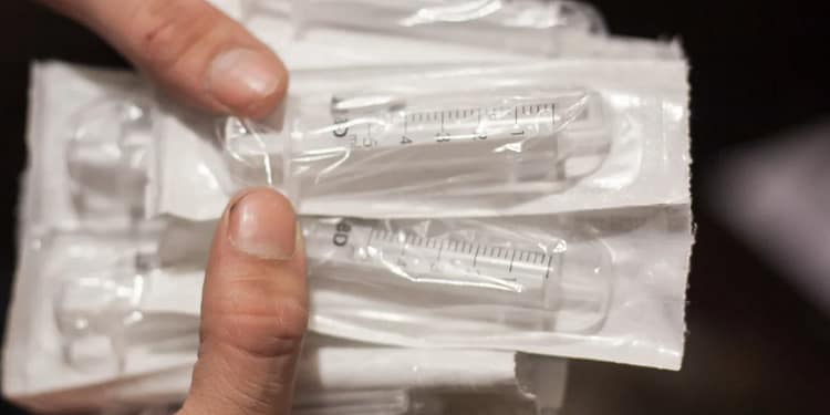 A hand holds a package of syringes in plastic wrap, several in a row, showing their measurement markings.