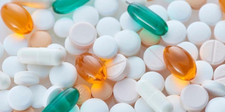 A variety of pills and capsules of different colors and shapes, including white, orange, and green tablets, arranged on a clear surface.
