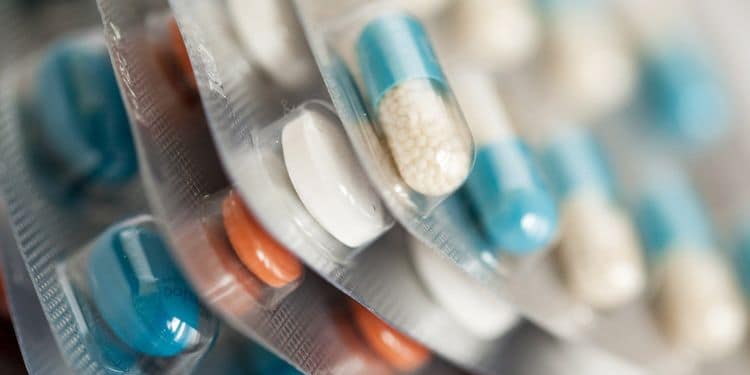 Paquetes de medicamentos con cápsulas de diferentes colores, incluidos azul, blanco y naranja, dispuestos en filas.
