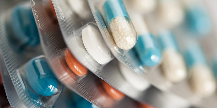 Packages of pills and capsules of different colors and shapes arranged in layers.