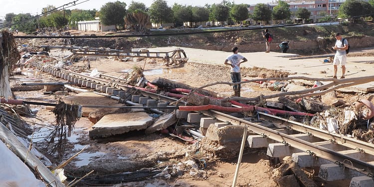 Image of a flood-affected area, with debris, pipes and damaged construction, and people inspecting the remains.