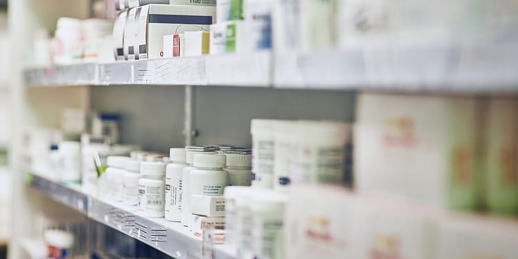Shelves in a pharmacy with various medicine containers, some embellished and others in white bottles. The image is slightly out of focus.